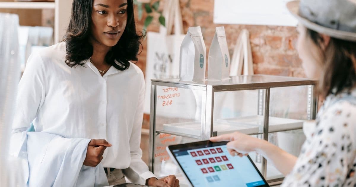 Une cliente en caisse devant un écran de paiement tactile s'apprête à présenter son mobile wallet sur smartphone